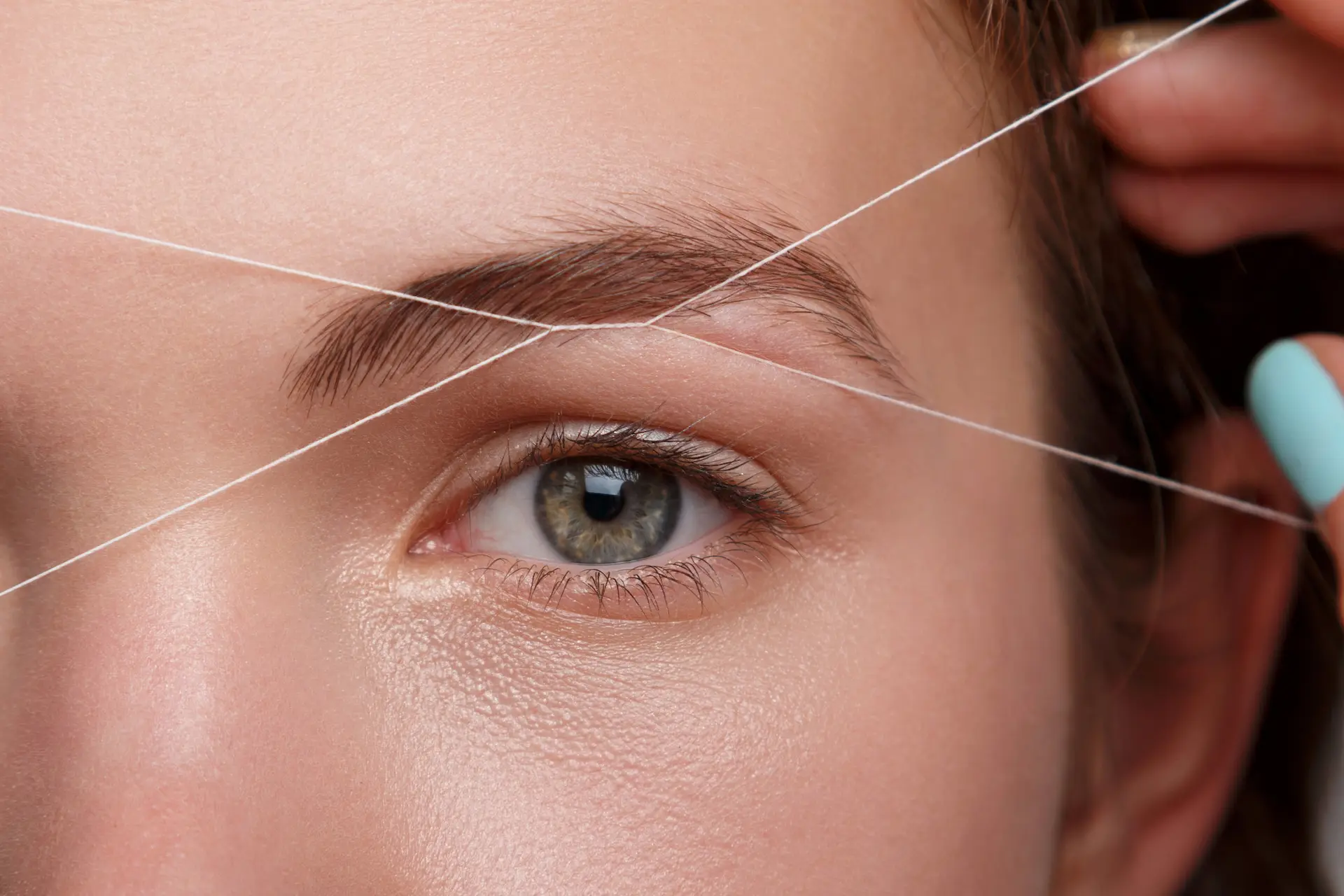 Mujer recibiendo depilación de cejas con hilo en Málaga